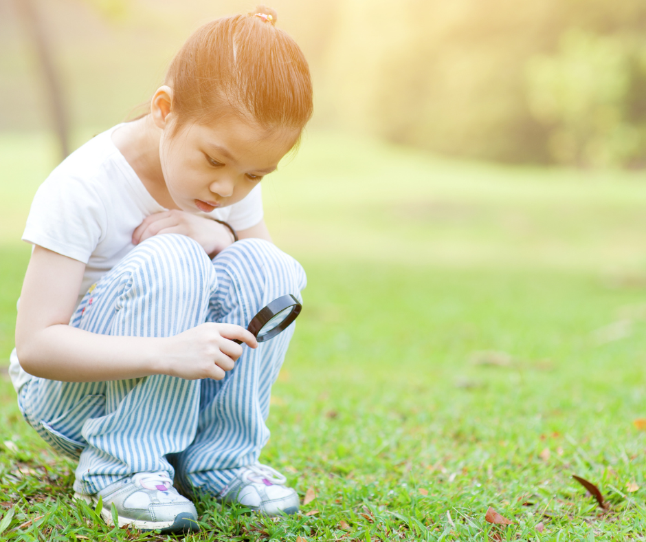 little girl looking at grass through a magnifying glass